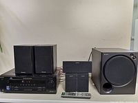 Complete home theatre system setup with Sony subwoofer, Sony receiver, Sony center and front speakers, Panasonic rear speakers, remote control in front.