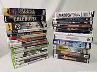 Two stacks of video games showing various titles and platforms including Xbox 360, PC, PS3, PSP, Wii, and Sega Genesis in original cases with visible wear.