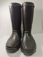 Front view of pair of tall black rubber winter boots with scuff marks and padded fleece lining visible at top.