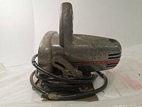 Side angled view of the Zephyr Model 411 circular saw showing metal body, handle, blade guard, base plate, and coiled power cord with frayed spots.