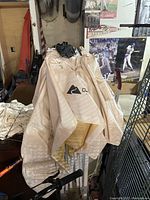 Photo showing folded large white weatherproof rain cover with logo and metal frame parts visible, in used condition.