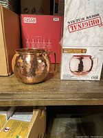 Side view showing a single hammered solid copper Moscow Mule mug next to its original branded box indicating 32 oz size and hammer texture.