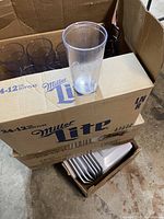 Boxes containing clear plastic Coca-Cola branded beverage cups, stacked and partially visible inside cardboard boxes.