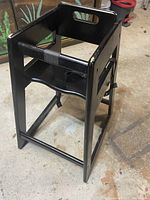 Black wooden highchair showing the seat, backrest with handle, and safety strap.