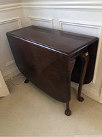 Closed view of the antique walnut drop leaf table showing the dark wood finish, curved legs and claw feet.