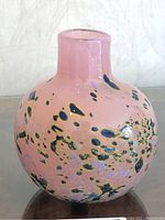 Front side view of pink art glass vase with blue and green decorative spots on a reflective surface.