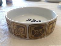 Side view of round ceramic wine coaster showing decorative geometric patterns in brown and gold squares around side surface.