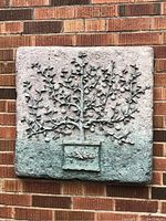 Front-facing photo of the square decorative wall plaque showing the raised tree design and textured background mounted on a brick wall.
