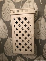 Front view of white lattice cabinet showing door and handle with distressed finish.