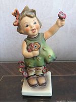 Front view of the porcelain Hummel figurine depicting a girl in a green dress holding red flowers.