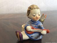 Close-up photo of Hummel ceramic angel candle holder sitting and playing guitar, showing the detailed hand-painted features and colors.