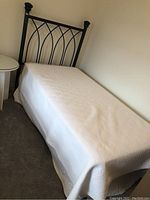 Full view of the single size bed with white bedspread, iron headboard visible at the end.