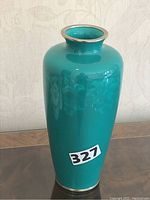 Full view of the green Japanese Ando cloisonne vase with silver rim and base sitting on a wooden surface.