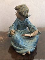 Front side view of the figurine showing detailed hair, face, blue robe, and the book resting on the right knee.