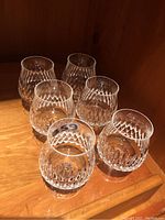 Six Nachtmann Desiree crystal beverage glasses displayed on a wooden surface with a diamond cut pattern and short stems, grouped together showing consistent design.