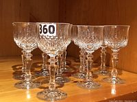 Eleven clear Nachtmann Desiree crystal goblets with textured cut pattern and faceted stems displayed on a wooden shelf.