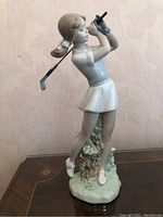 Front side view of the NAO by Lladro figurine showing the female golfer in mid-swing on a decorative base