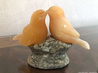 Front view of two orange onyx lovebird figurines close together on gray marble base showing natural markings.