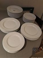 Multiple stacks of white ceramic plates arranged on table, showing four distinct groups of plates varying in size indicating different plate types included.