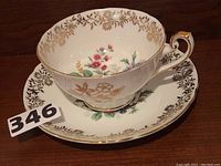 Porcelain teacup on matching saucer with floral patterns and gold accents.