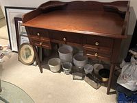 Front view of the desk showing raised gallery back, five drawers with brass ring pulls, turned legs, and surrounding items
