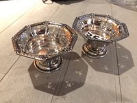 Two octagonal sterling silver footed sweetmeat dishes with pierced sides and floral rim decorations seen side by side.