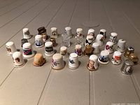 Front view of various ceramic, metal, and souvenir thimbles arranged on table, showing diverse colors and designs including floral and portrait imagery.