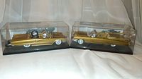 Two golden Cadillac Eldorado Biarritz convertible model cars in clear display cases with black bases, positioned side by side.