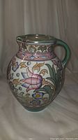 Full view of hand painted ceramic pitcher with floral and geometric designs, showing the front side and handle.