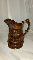 Front view of antique gold lustre pitcher showing ballerina relief and handle design.