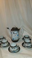 Full view of antique Japanese Kutani tea set, including the teapot and five cups with saucers all arranged on cloth backdrop.