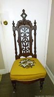 Full view of antique Victorian chair showing carved wooden back, turned posts, finials, and yellow needlepoint upholstered seat with floral design.