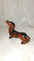 Front-side angle of the 4.5 inch porcelain dachshund figurine with black and brown glaze on white background.