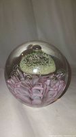 Front view of the hand-blown glass paperweight showing the green flower and pink petals with bubbles inside.