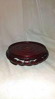 Front and slightly elevated angled view of the circular Chinese rosewood wood stand on a plain white background. Shows the top surface and carved ornamental sides.