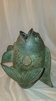 Side view of the bronze fish statue showing detailed scales, fins, open mouth, and green patina finish.