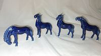Four blue glaze porcelain horse figurines shown from side angle, displaying varied poses and deep blue glaze.