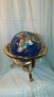 Full view of globe mounted on brass tripod stand against neutral background