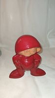 Front view of the red gnome figurine showing the large hood, facial features, arms akimbo posture.