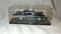 Side view of black vintage style model car inside clear plastic display case showing car details and base.