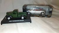 Close-up side view of green 1941 Plymouth pickup model truck on black stand.