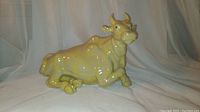 Front angle view of the porcelain cow statue on a white cloth backdrop showing yellow coloration and detailed facial features.