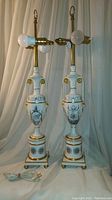 Full view of both porcelain Greco-Roman style lamps with double handles, gold accents, dual bulb brass fixtures, and cords with extra switches.