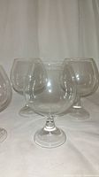 Four clear crystal glasses suitable for wine or brandy displayed on white backdrop, showing rounded bowls and short stems.