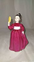 Front view of Royal Doulton Vanity girl figurine, holding yellow hand mirror, dressed in burgundy dress with white sash.