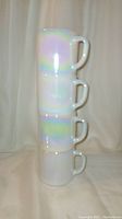 Stacked view of four Foster USA iridescent milk glass mugs showing their rainbow finish and rounded handles.