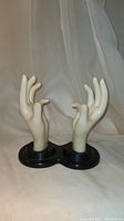 Pair of vintage lifesize mannequin hands positioned upright on a connected dual black base, against a white fabric backdrop.