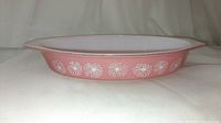 Full side profile of the pink Pyrex casserole dish showing white daisy pattern around sides