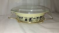 Front view of vintage Pyrex casserole in stand with glass lid, showing food graphic design around sides.