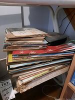 Stack of vinyl records with visible wear to sleeves, on white shelf.